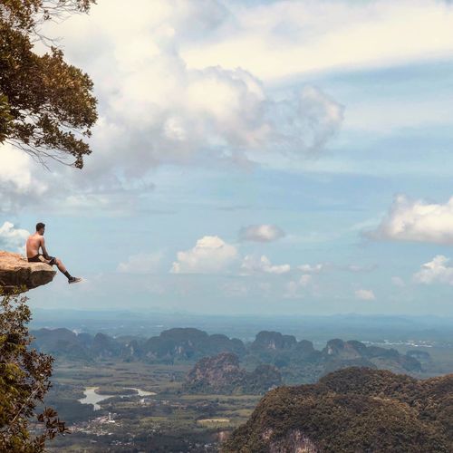 Shirtless man sitting on mountain against sky