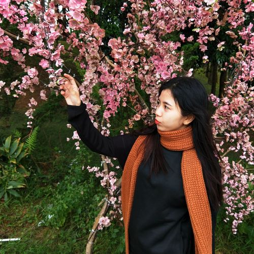 Young woman with pink flowers against trees
