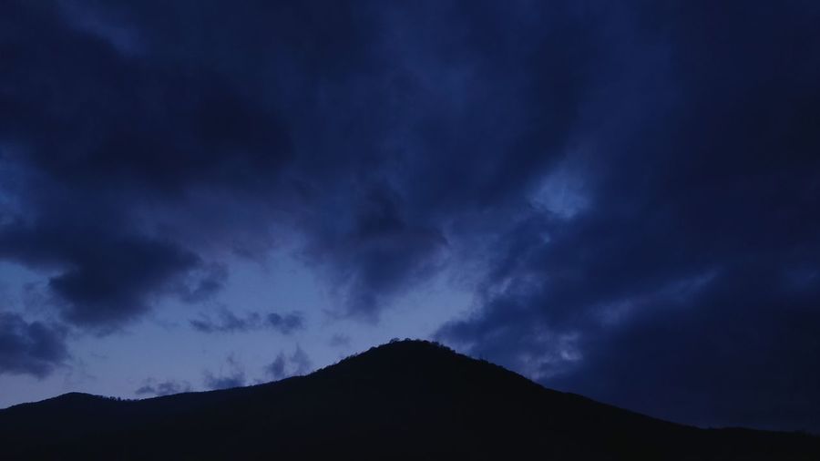 Low angle view of silhouette mountain against storm clouds