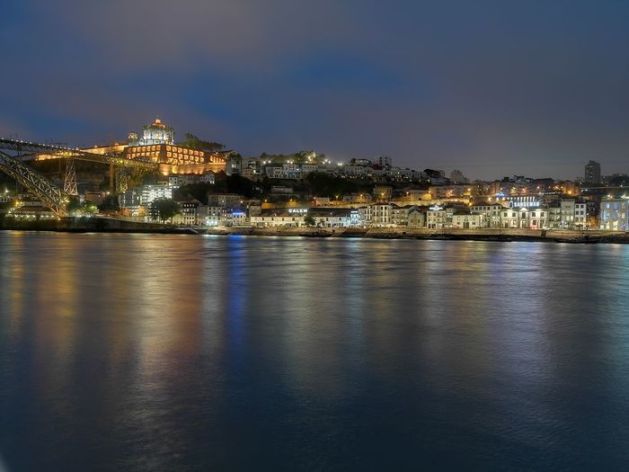 Illuminated buildings by river against sky at night