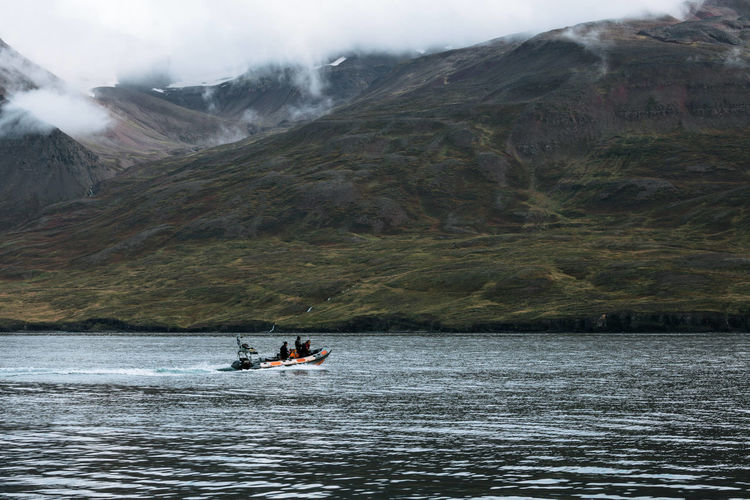 People on boat in lake against mountains