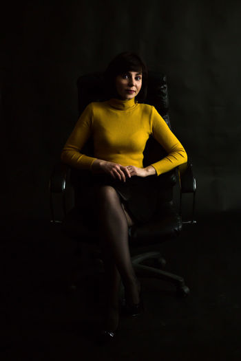 A brunette woman in bright yellow turtleneck behind huge leather chair.