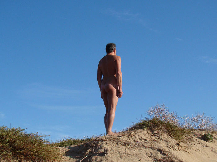 Low angle view of naked man standing against blue sky