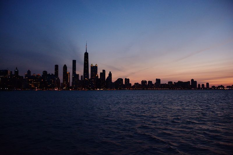 Sea with buildings in background at sunset