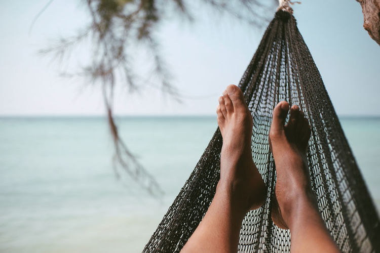 Low section of woman on hammock at beach against sky