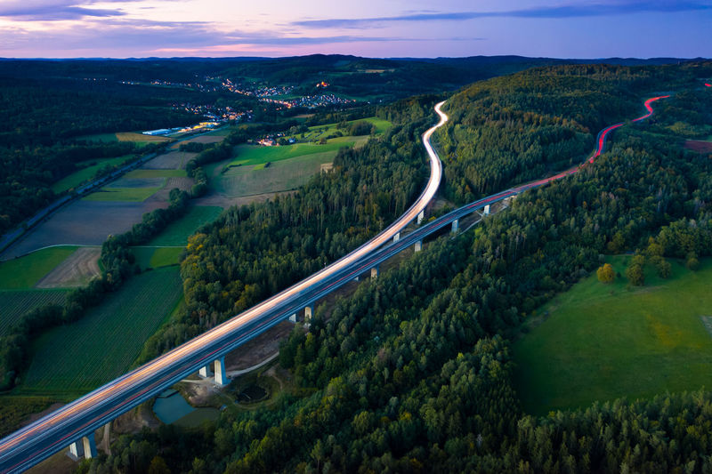 Aerial view of highway splitting aound forest hill on autumn evening