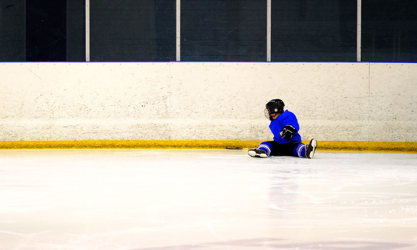Full length of player sitting on ice hockey rink