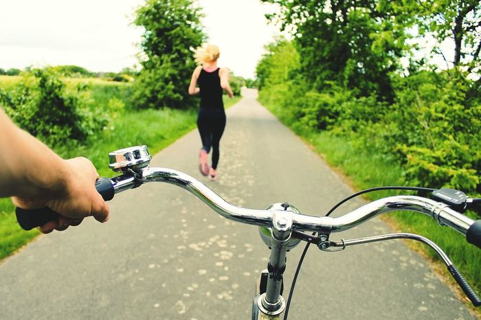 Close-up bicycle handlebar with woman running in distance