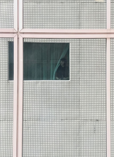 Reflection of a woman looking out of a window, in a wall with small, square tiles and pink stripes