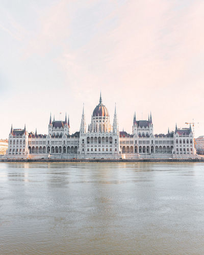 Hungarian parliament building by river against sky