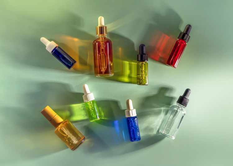Transparent glass dropper bottles with colorful liquids on green background. cosmetics, healthcare