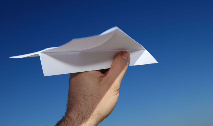 Cropped hand of paper airplane against clear blue sky