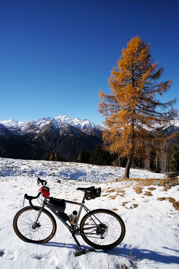 Bicycle on field by snowcapped mountain against blue sky
