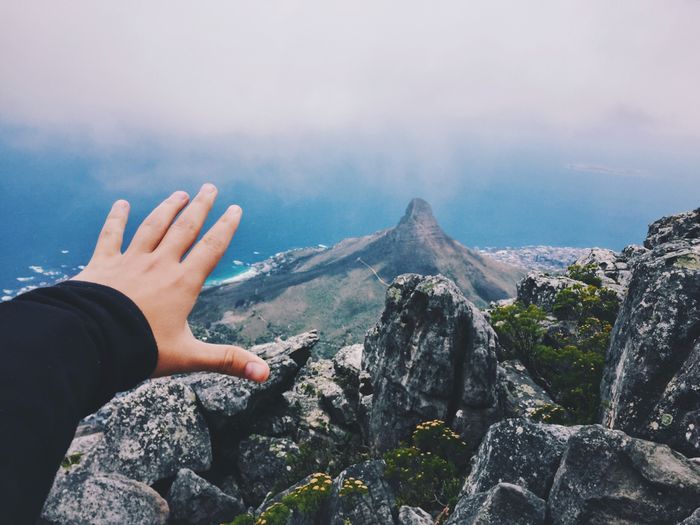 Person reaching towards mountain against sky