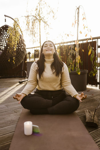 Smiling woman practicing lotus position on exercise mat at terrace