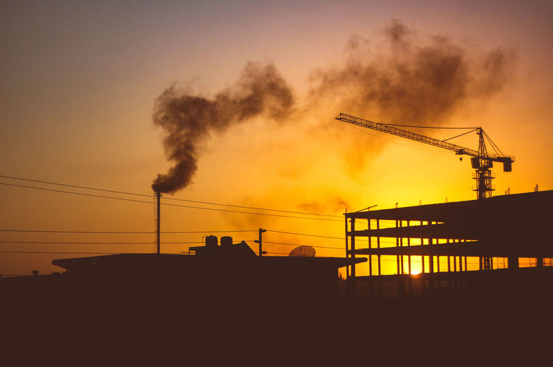 Silhouette cranes against sky at sunset