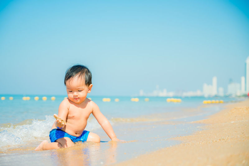 Full length of shirtless boy on beach against sky