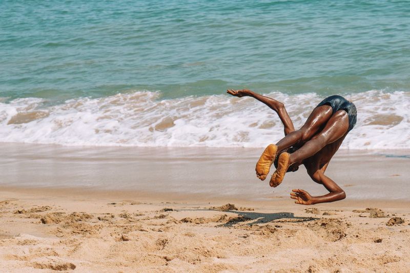 Shirtless man jumping on beach