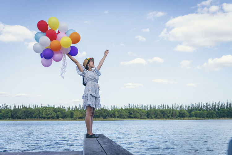 Full length of woman standing on balloons against sky