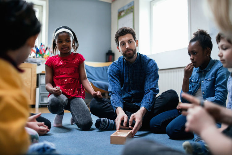 Teacher playing with children while sitting in classroom