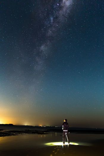 Rear view of man standing on illuminated beach against starry sky