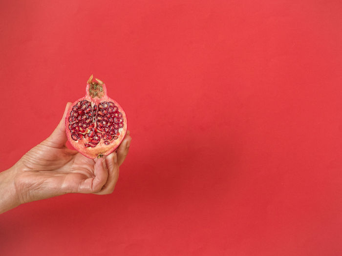Midsection of person holding strawberry against red background