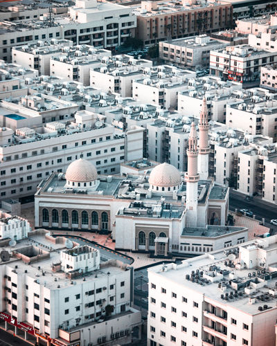 A white mosque in an urban city surrounded by apartment buildings, with the dome and minaret