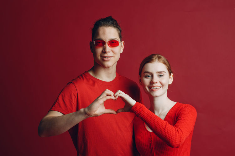 Portrait of smiling couple making heart shape against red background
