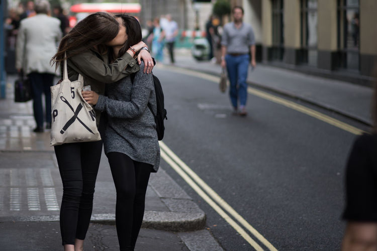 Lesbian couple kissing while walking on sidewalk