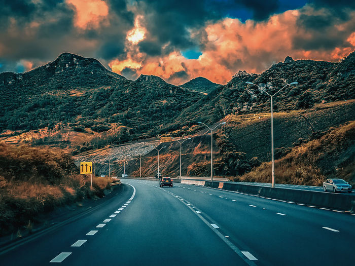 Road by mountains against cloudy sky during sunset