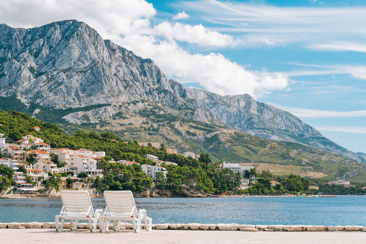 Deck chairs at beach against scenic view of sea and biokovo mountains