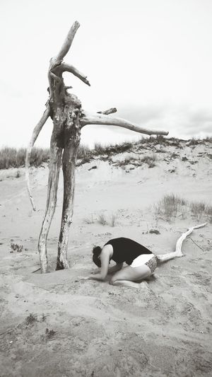 Woman kneeling in front of dead tree at beach