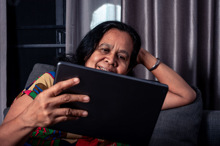 Smiling woman watching movie on digital tablet at home