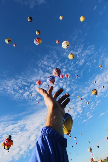 Optical illusion of hand touching hot air balloons flying against sky