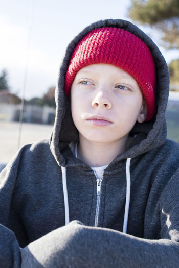Thoughtful boy wearing knit hat and hooded shirt while looking away