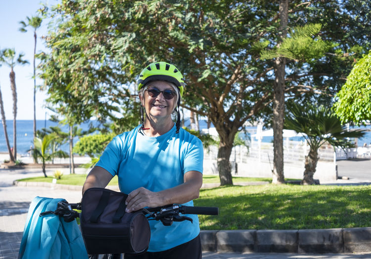 Portrait of senior woman standing by bicycle against trees