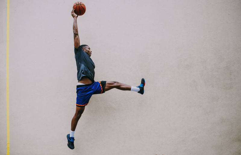Young man playing basketball against wall