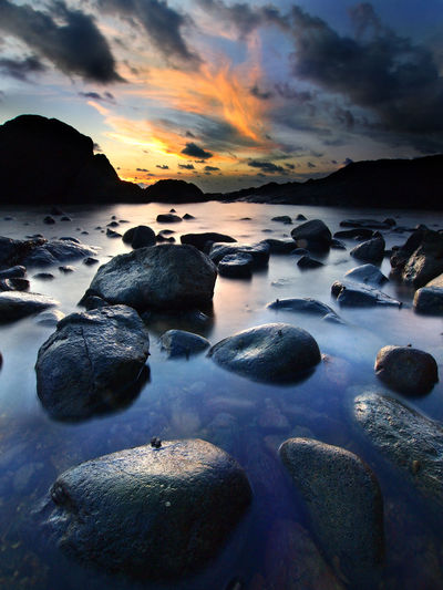 Rocks at sea shore against sky during sunset