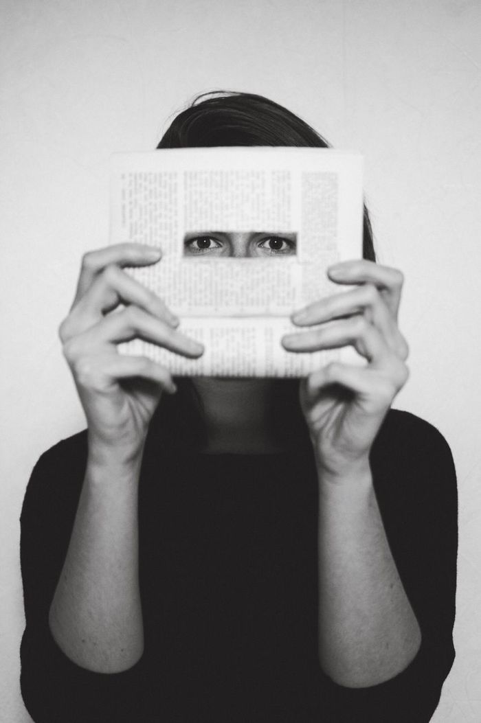 Portrait of woman holding book with hole while standing on white background