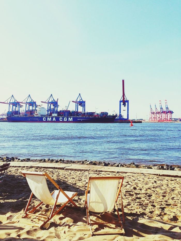 Container ship docked at port with empty deck chairs in foreground