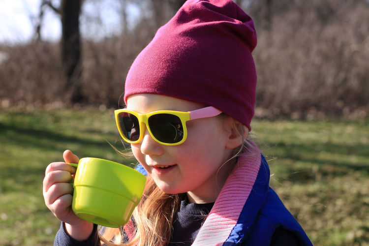 Smiling child in colorful clothes drinking tea in green reusable cup. eco-friendly family picnic.