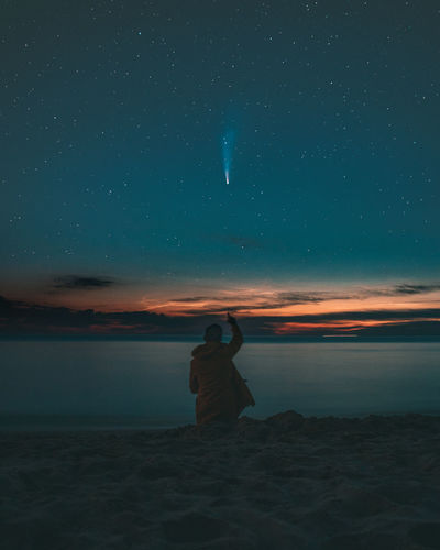 Rear view of man on beach against sky at night