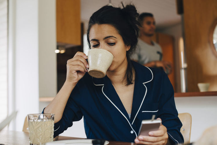 Woman drinking coffee while looking at glaucometer by table