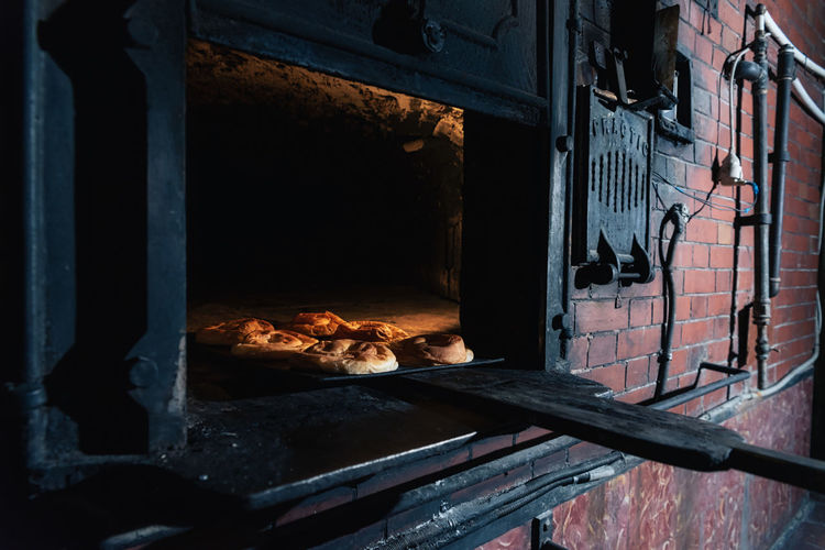Set of fresh buns placed inside hot brick oven in professional bakery