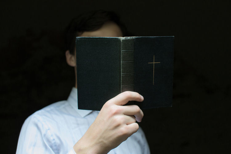 Close-up of man reading bible against black background
