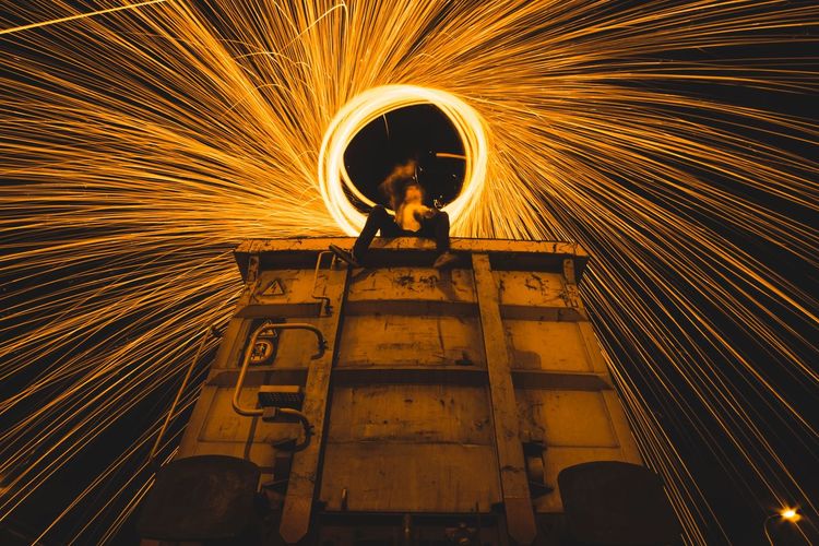 Low angle view of person sitting on train while spinning fire steel wool at night