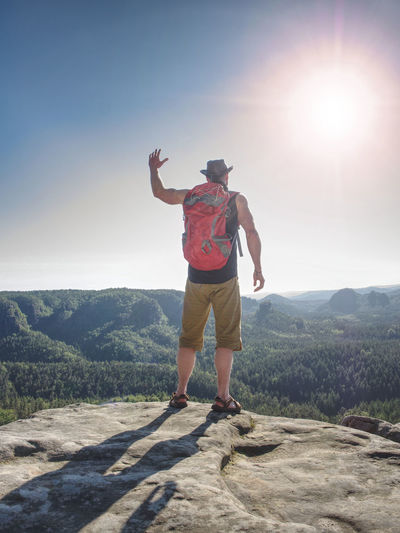 Traveler guy wears light shorts, black leather vest and leather crimson hat. sun shine on his figure