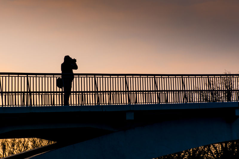 Silhouette person standing on footbridge against clear sky