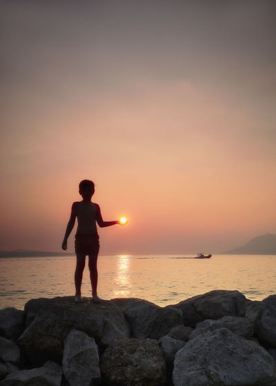 Full length of boy standing on rock at beach during sunset
