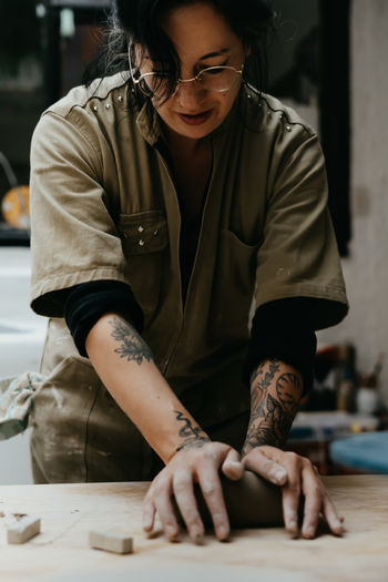 Focused female artisan with dirty hands shaping clay on table while creating pottery in workshop
